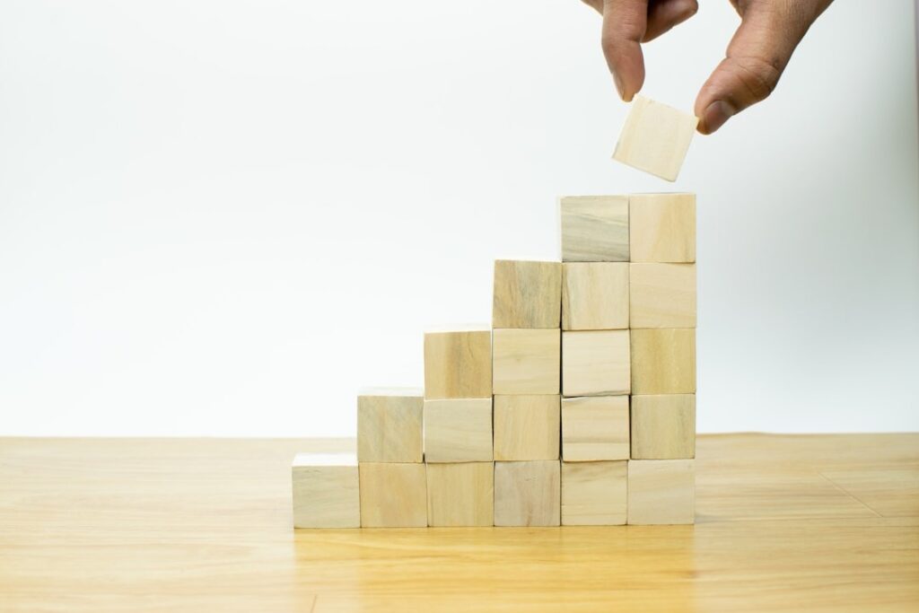 A hand placing the final wooden block on top of a staircase-like structure made of cubes, symbolizing growth and progress, representing how Eunika Agency builds digital strategies for business success.